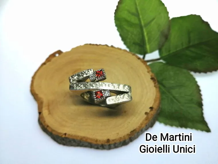 Un anello lavorato a mano appoggiato su una fetta di legno, accanto a delle foglie