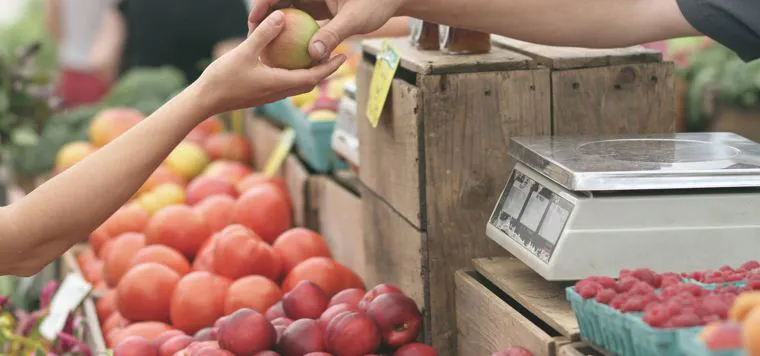 Un banco di mele al mercato, con la bilancia e la mano di chi serve